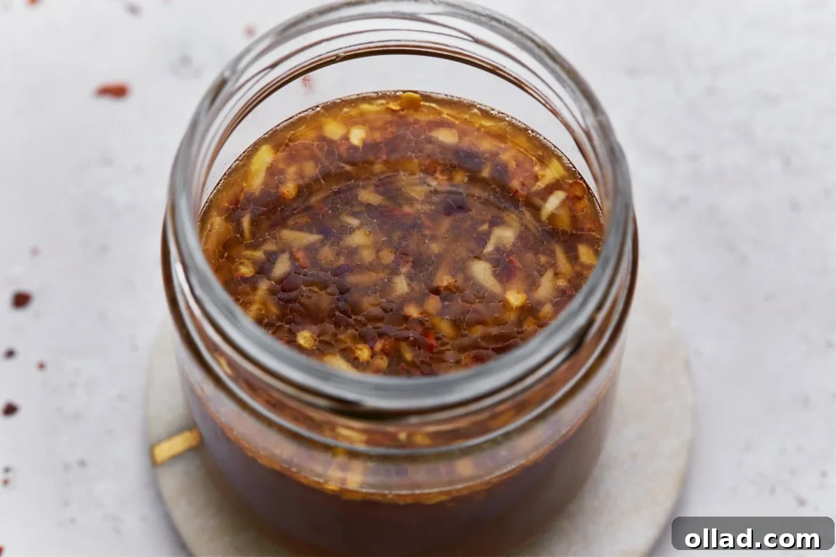 A close-up of gluten-free stir-fry sauce in a jar, highlighting the garlic, chili flakes, and glossy liquid that make the sauce appealing