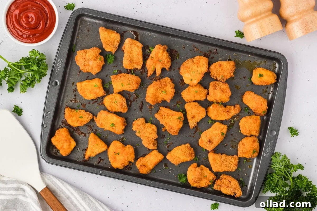 Freshly baked gluten-free chicken nuggets on a baking sheet, golden brown and garnished with chopped parsley.