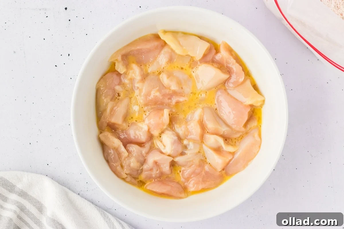Bowl of chicken nugget pieces coated in beaten egg, prepped for breading.