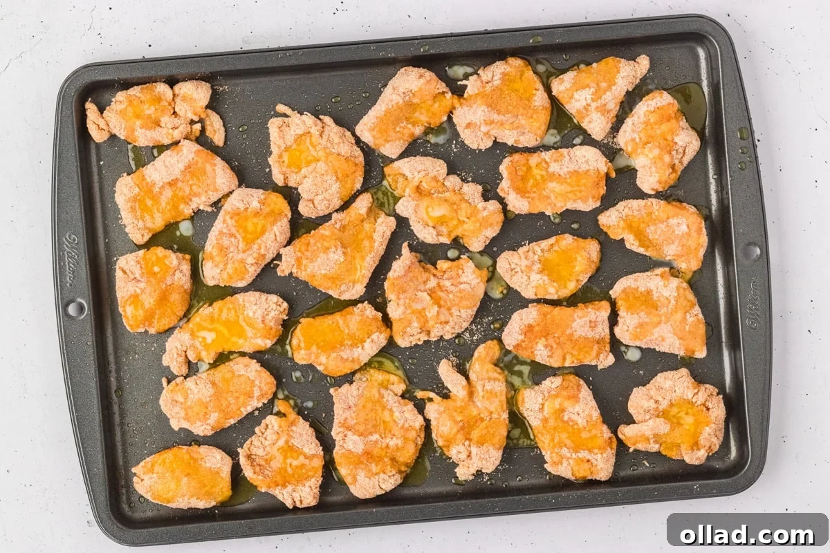 Breaded chicken nuggets arranged on a baking sheet, drizzled with melted butter, before baking.