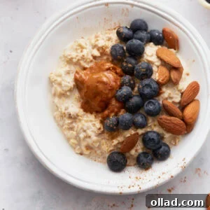 A bowl of creamy gluten-free overnight oats topped with fresh blueberries, whole almonds, and a dollop of almond butter, sprinkled with cinnamon, on a light surface.