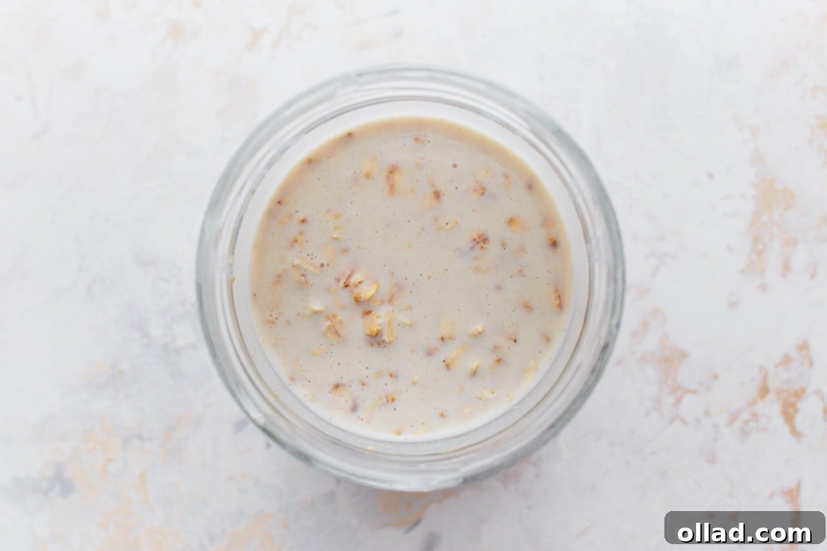 A glass jar containing gluten-free overnight oats soaking in creamy liquid, ready to be chilled.