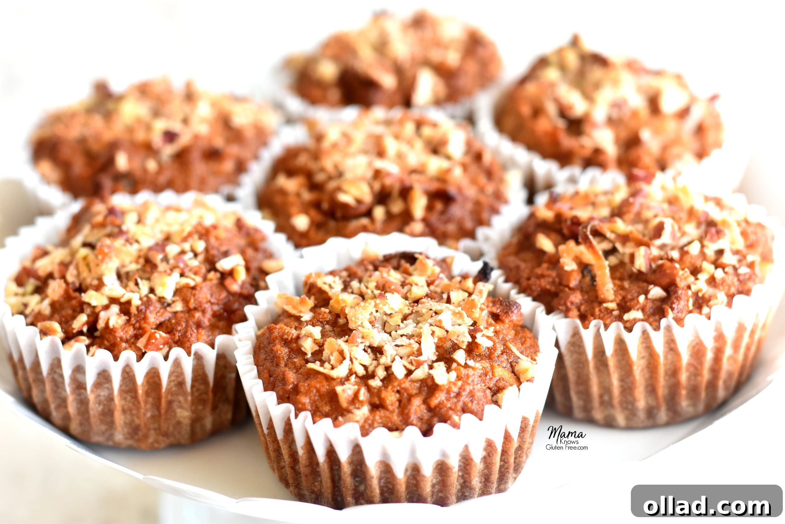 Paleo Carrot Cake Muffins Gluten Free Dairy Free Refined Sugar Free 3 Seven golden-brown Paleo carrot cake muffins neatly arranged on a pristine white cake stand, showcasing their inviting texture and rustic charm.