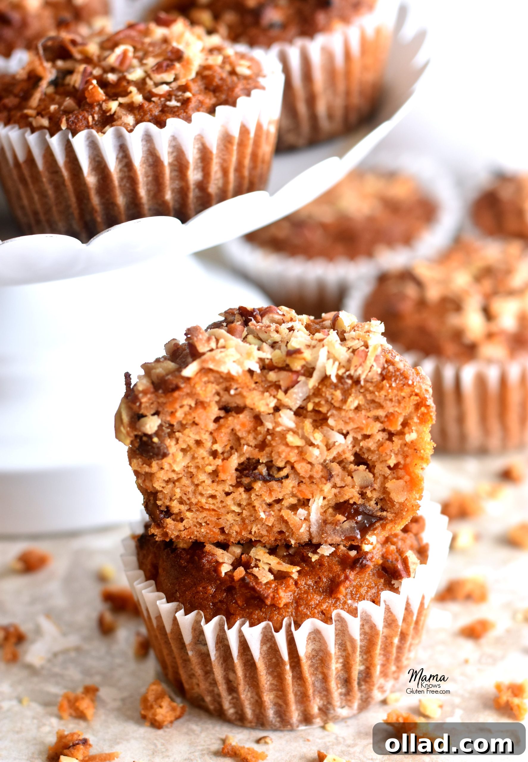 Paleo Carrot Cake Muffins Gluten Free Dairy Free Refined Sugar Free 4 A Paleo carrot cake muffin, cut in half to reveal its moist interior packed with shredded carrots, raisins, and pecans, stacked on top of a whole muffin with more in the background, emphasizing its tempting texture.