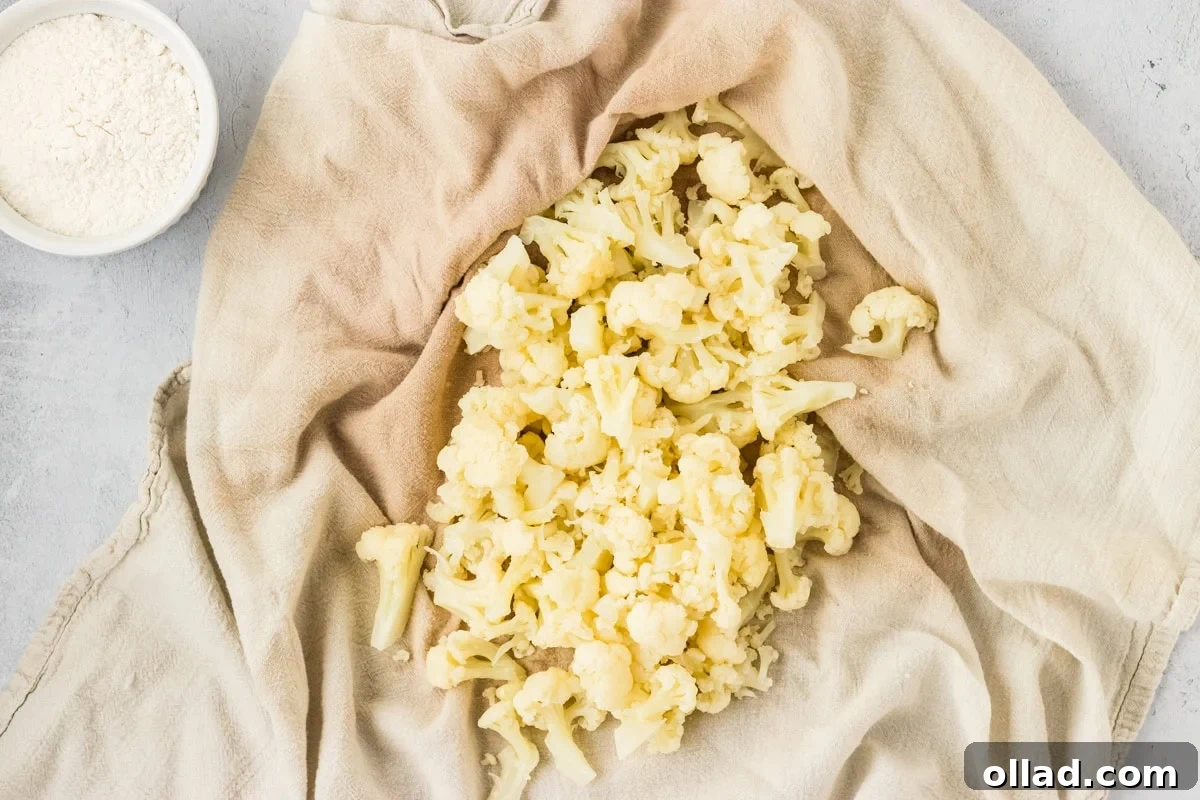 Pillowy Homemade Cauliflower Gnocchi 6 A clean kitchen towel containing a mound of cooked and thoroughly drained cauliflower florets. The towel is gathered, ready to be squeezed to remove any remaining excess moisture, a critical step for perfect cauliflower gnocchi.