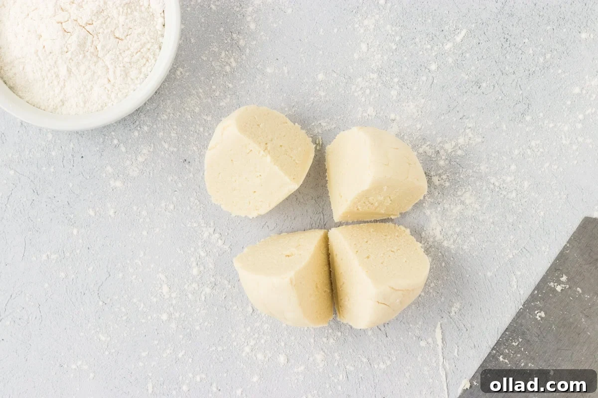 Pillowy Homemade Cauliflower Gnocchi 9 A single, smooth ball of cauliflower gnocchi dough has been expertly divided into four equal portions, arranged neatly on a lightly floured work surface. This clear segmentation makes the next step of rolling and shaping much easier.