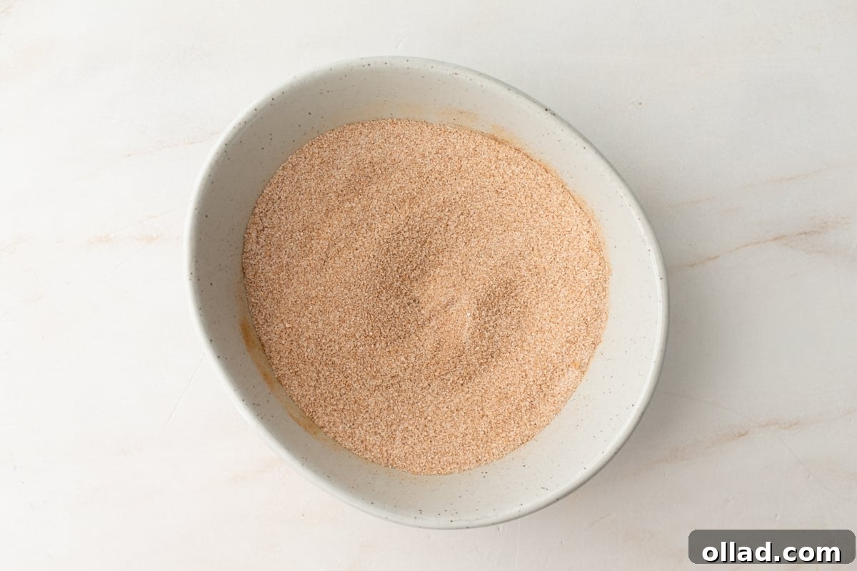 A white ceramic bowl filled with a cinnamon sugar mixture, showing its fine, sandy texture, ready for coating the donuts.