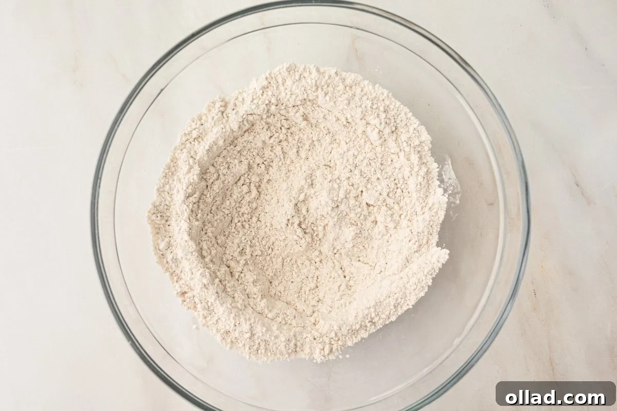 A glass mixing bowl with whisked dry ingredients, including gluten-free flour and spices, creating a light, airy mixture before combining with wet ingredients.