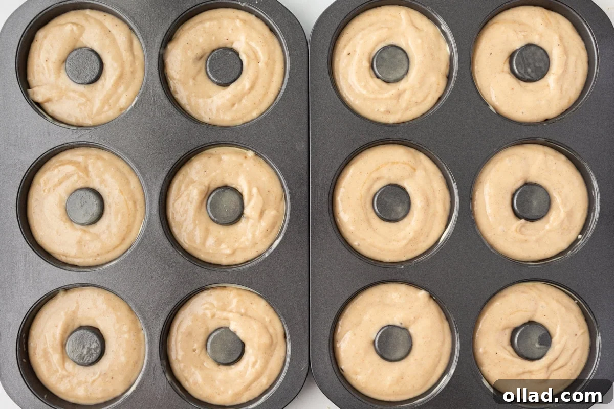 Donut batter piped into a greased donut pan, showing the smooth, thick consistency of the gluten-free mixture before baking.
