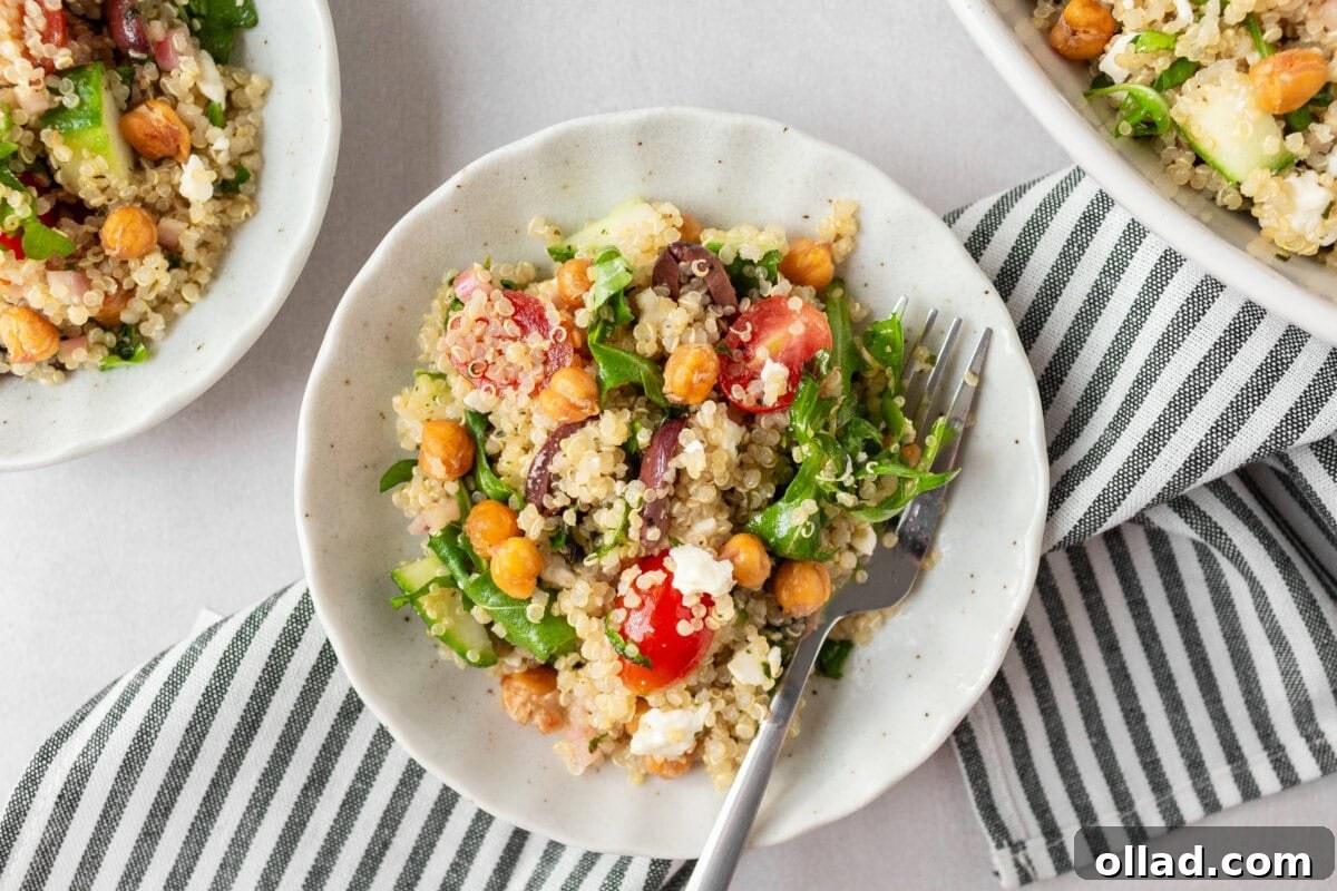 Mediterranean Quinoa Bowl 11 Small white bowls filled with Greek quinoa salad, ready to be served, with a striped napkin underneath and a fork resting in one bowl.