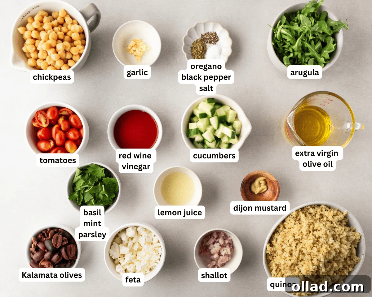 Mediterranean Quinoa Bowl 4 Greek quinoa salad ingredients laid out on a white surface, including cooked quinoa, fresh arugula, chopped cucumbers, halved cherry tomatoes, Kalamata olives, crumbled feta, fresh herbs, roasted chickpeas, and a jar of homemade vinaigrette.