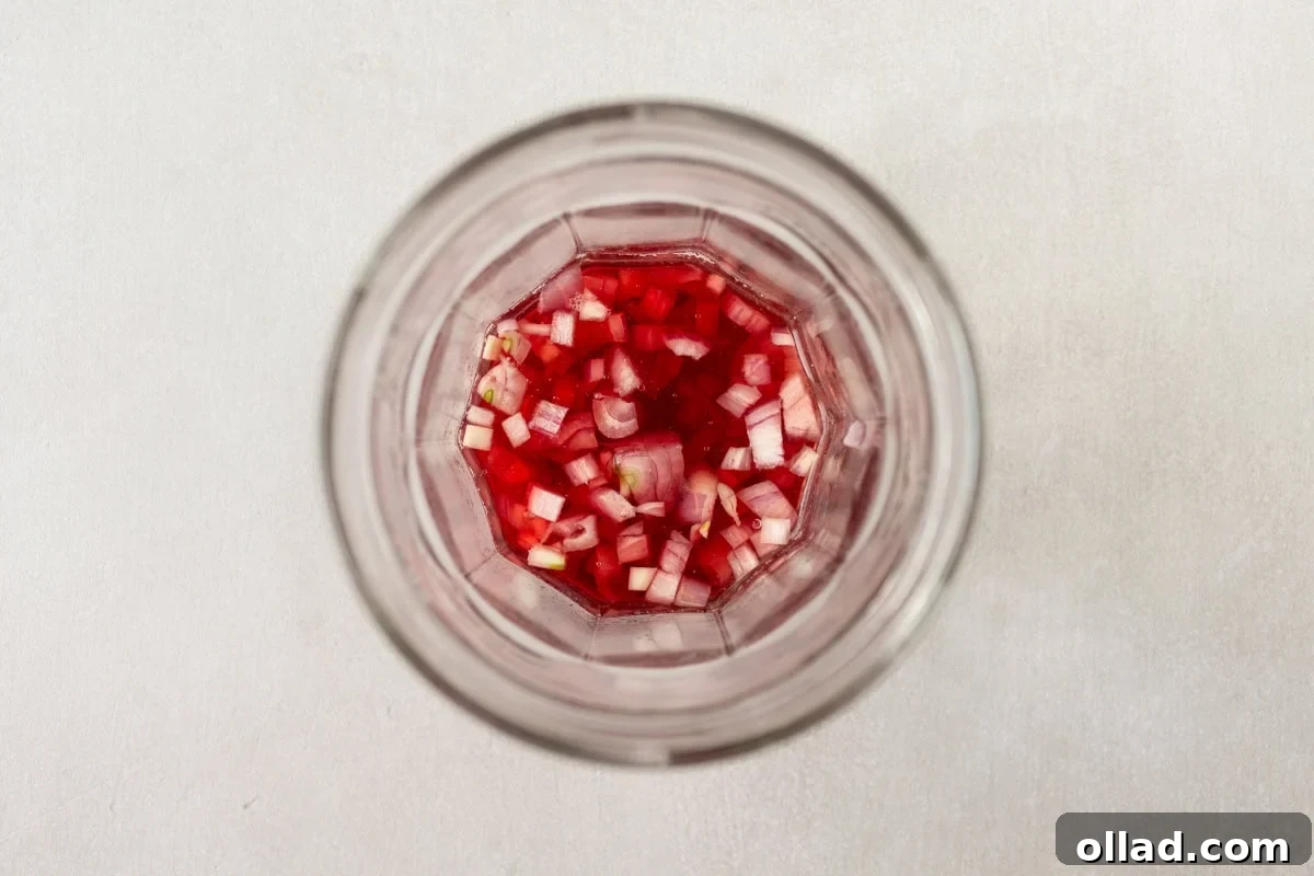 Mediterranean Quinoa Bowl 5 A close-up overhead shot of a glass jar filled with finely diced red onions soaking in a red liquid, likely vinegar, for pickling, preparing for the vinaigrette.