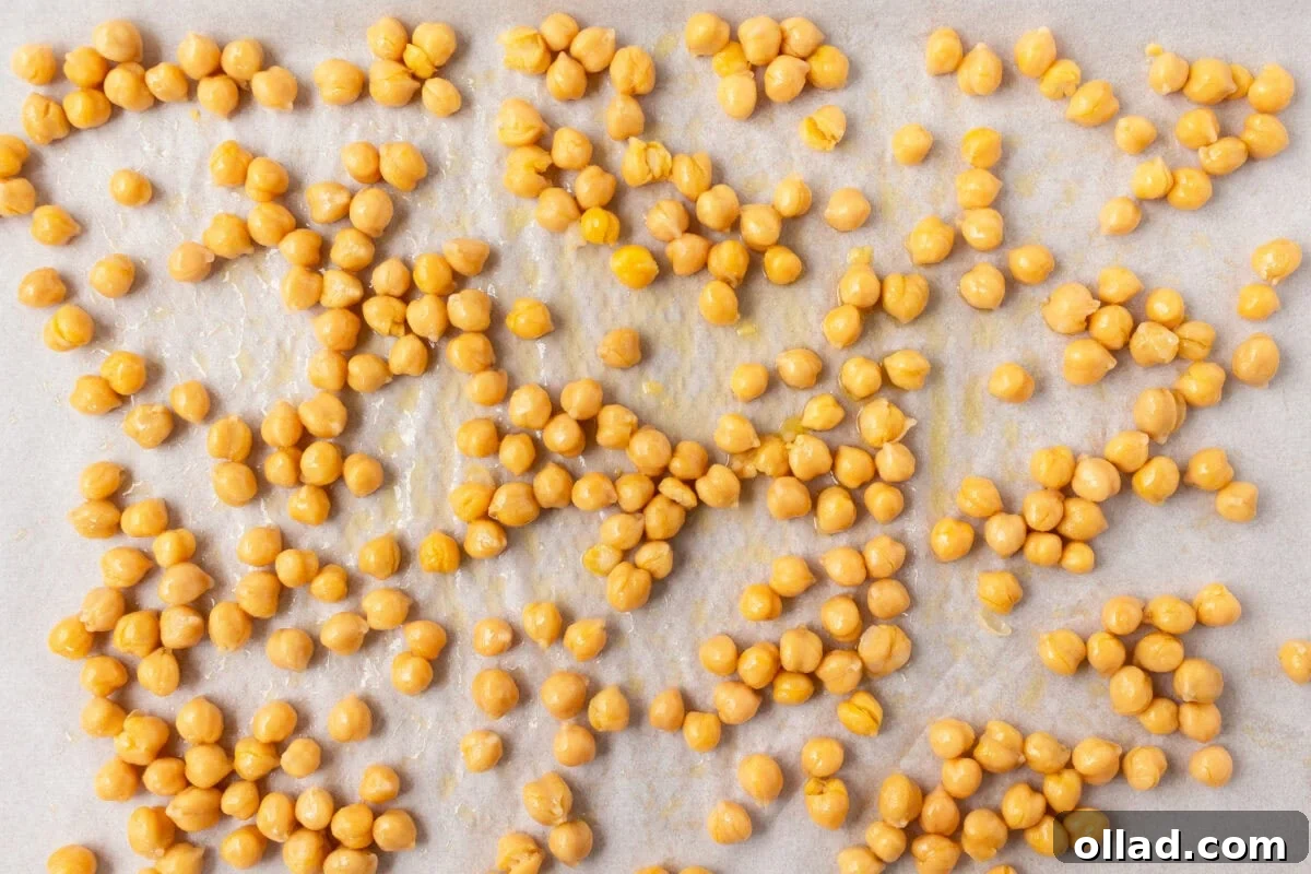 Mediterranean Quinoa Bowl 8 A parchment-lined baking sheet with chickpeas coated in olive oil and salt, evenly spread out before roasting.