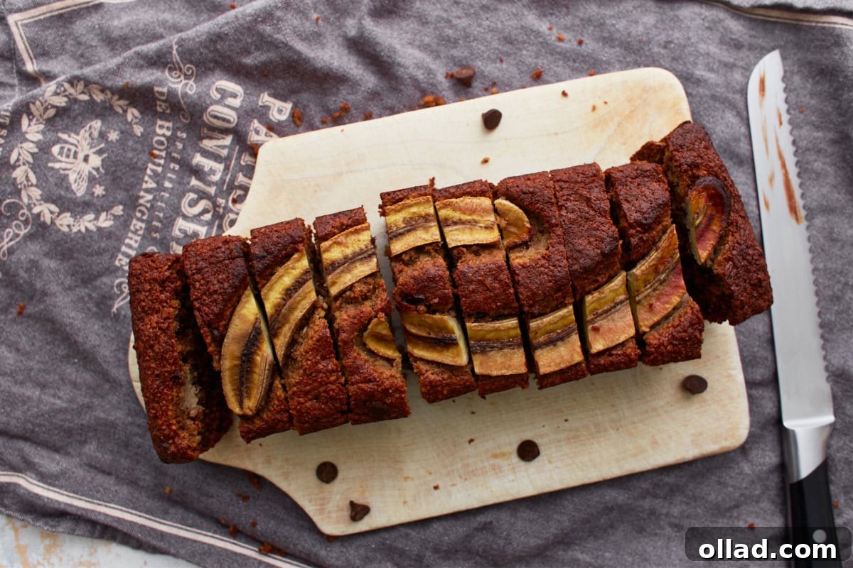 Wholesome Gluten-Free Banana Oat Loaf 11 A top-down view of a fully sliced loaf of banana oatmeal bread on a wooden cutting board, with a serrated knife nearby.