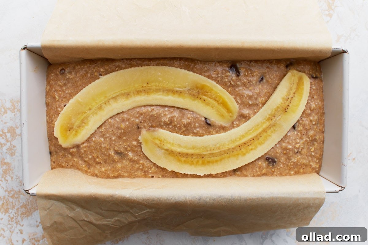 Wholesome Gluten-Free Banana Oat Loaf 9 A parchment-lined loaf pan filled with banana bread batter, topped with two long banana slices.