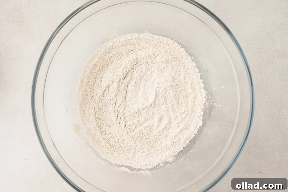 A glass mixing bowl holds a perfectly blended mixture of dry ingredients for cassava flour tortillas, showcasing the fine, uniform consistency of the flours and seasonings.