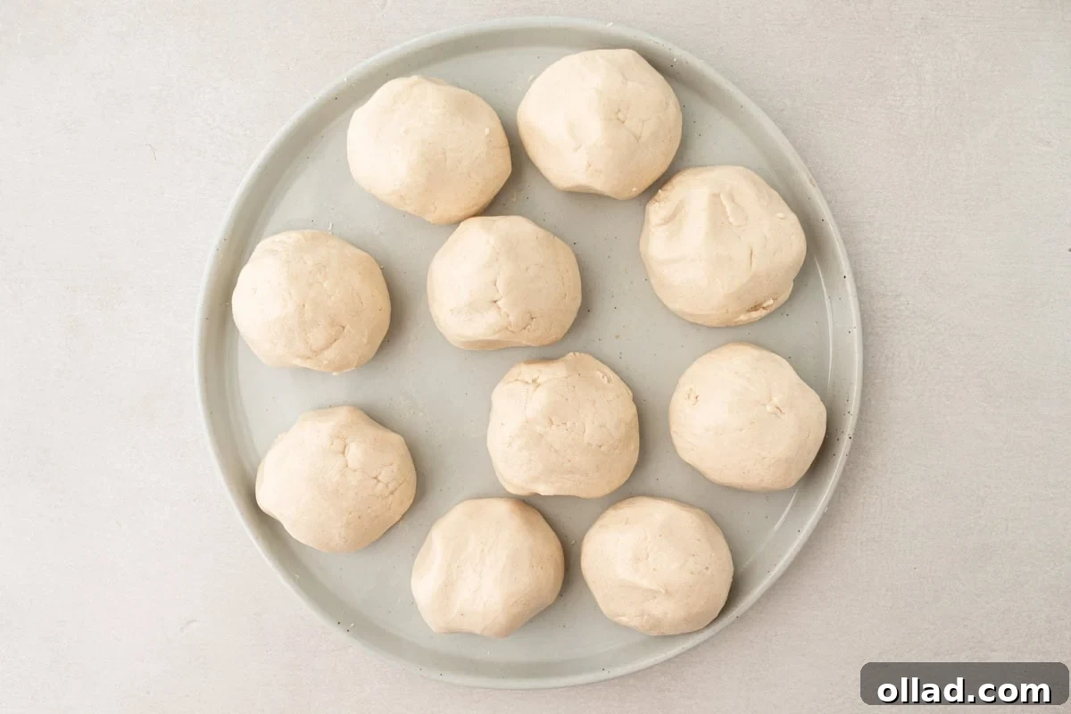 Ten perfectly portioned dough balls, uniformly spaced, rest on a round plate, covered with a damp towel to maintain moisture and pliability before shaping into tortillas.