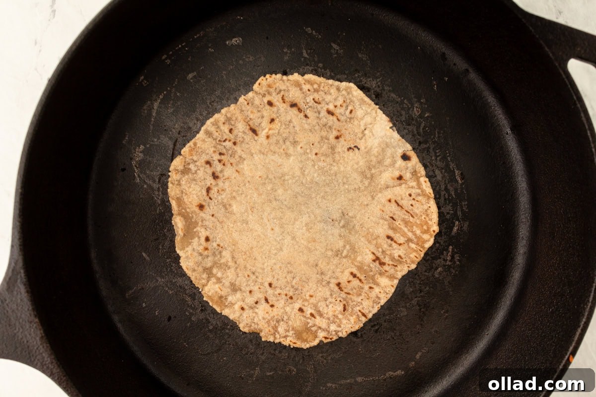 A cassava tortilla cooks to golden perfection in a black cast-iron skillet, revealing enticing light browning and subtle bubbly textures on its surface.