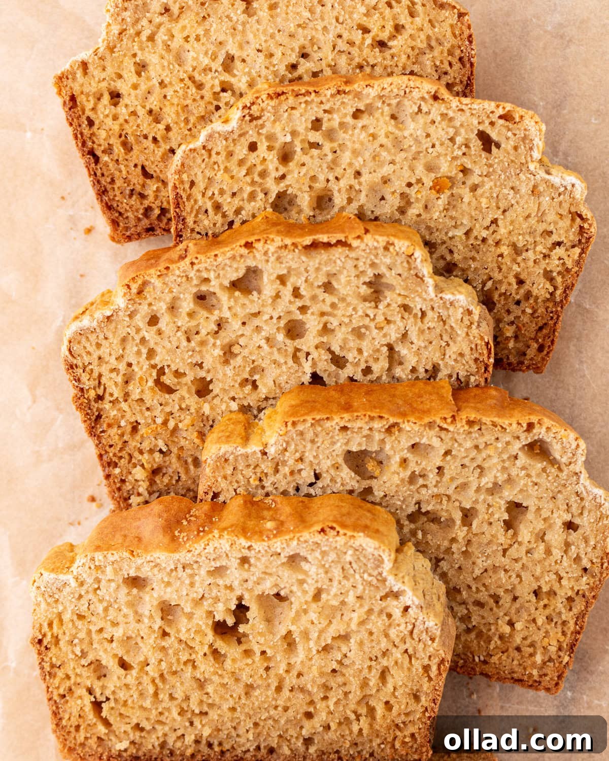 Yuca's Rustic Bake 2 Overhead view of several golden-crusted, airy cassava bread slices arranged on parchment paper.