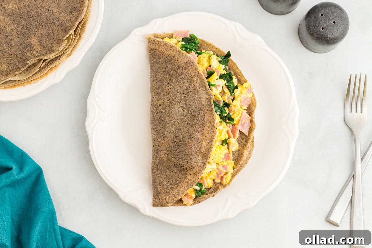 Buckwheat Galettes 11 A buckwheat crepe folded in half and filled with scrambled eggs, ham, and sautéed spinach on a white plate, with salt and pepper shakers and utensils nearby.