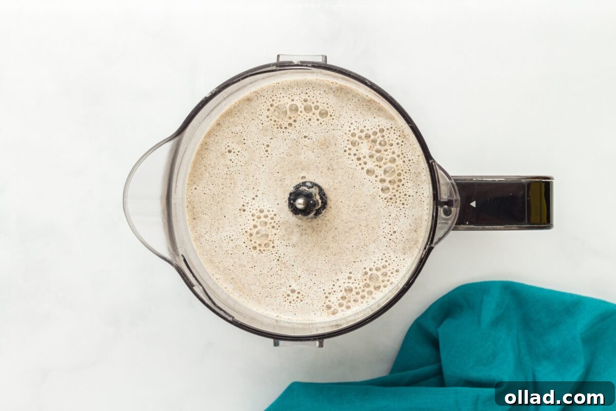 Buckwheat Galettes 5 A blender filled with frothy buckwheat crepe batter, resting on a white surface next to a teal napkin.