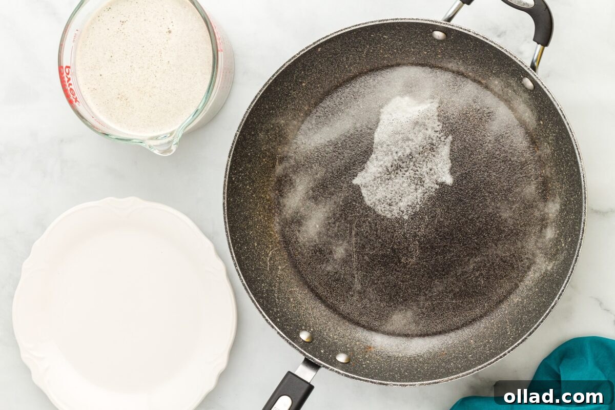 Buckwheat Galettes 6 A non-stick frying pan sprayed with cooking oil, sitting next to a measuring cup of crepe batter and an empty white plate.