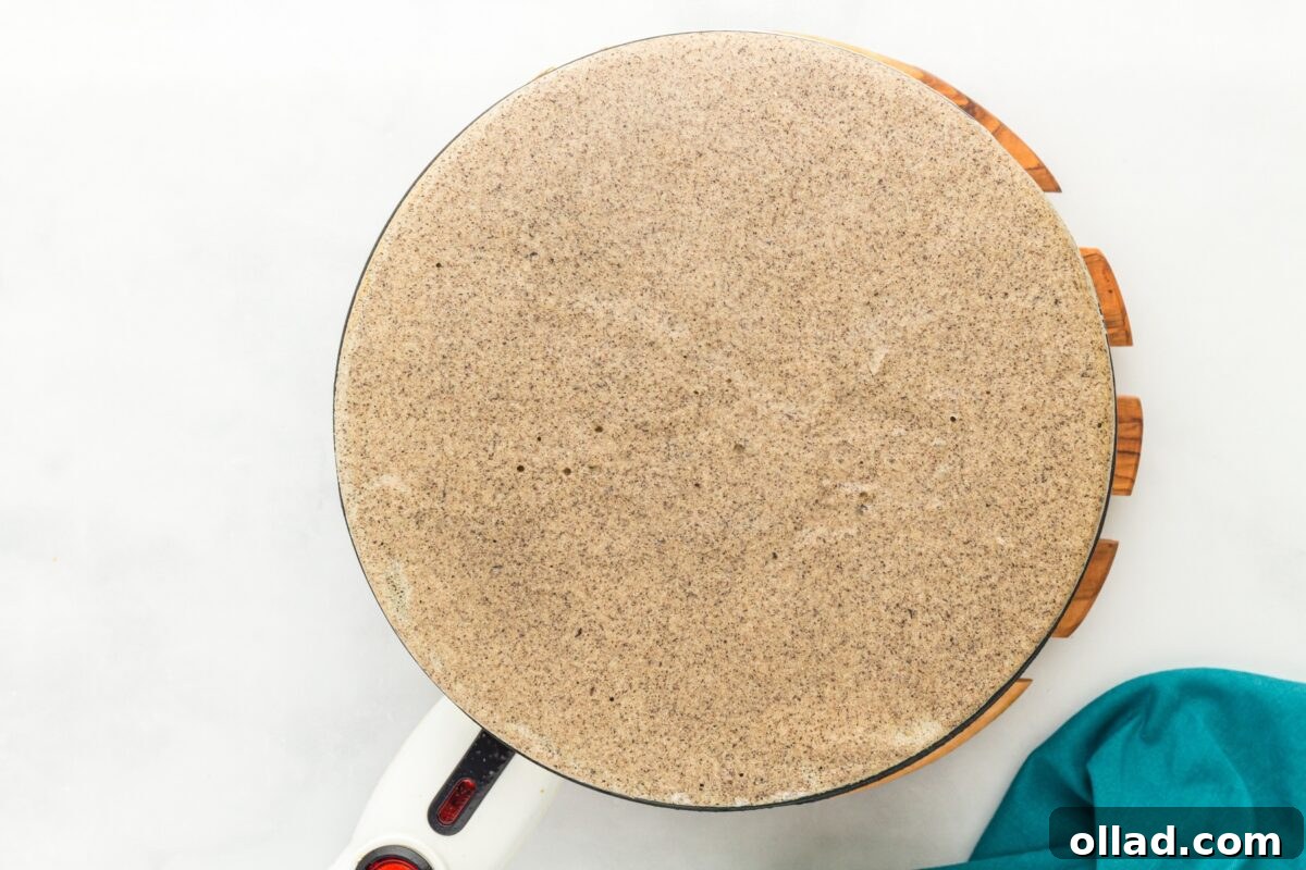 Buckwheat Galettes 9 A thin buckwheat crepe cooking on an electric crepe maker with a smooth, round surface.