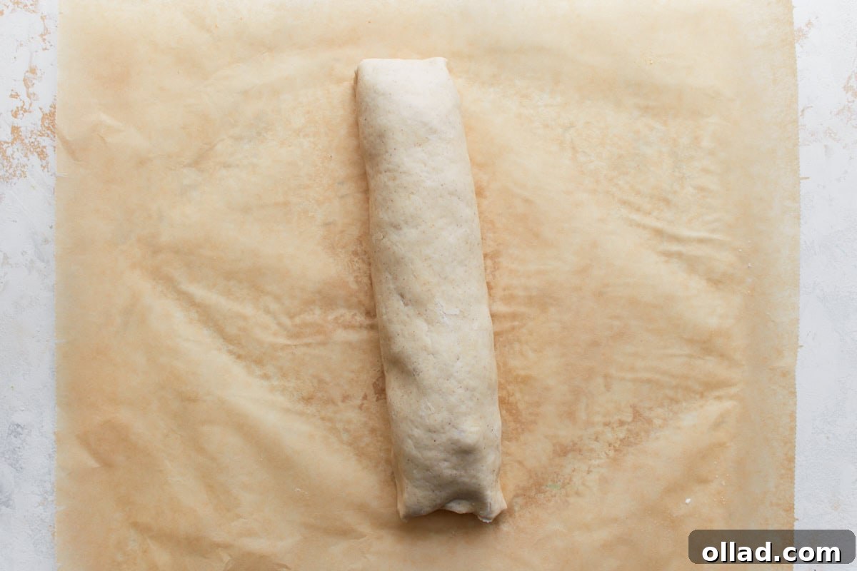 Irresistible Gluten-Free Pizza Poppers 9 Rolled-up log of pizza dough filled with toppings, placed seam-side down on parchment paper.