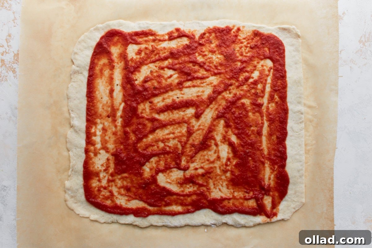 Irresistible Gluten-Free Pizza Poppers 7 Rectangular dough topped with an even layer of red pizza sauce, leaving a border around the edges.