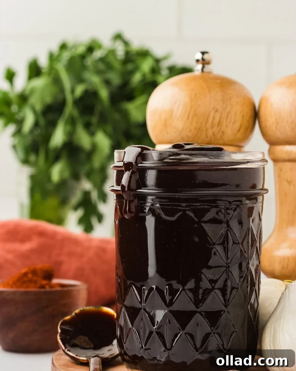 Crafted Gluten-Free BBQ Sauce 2 A glass jar filled with thick, dark homemade gluten-free BBQ sauce, with sauce dripping slightly over the rim. Fresh parsley, garlic cloves, and wooden pepper mills are artfully arranged in the background, hinting at fresh ingredients and culinary delight.
