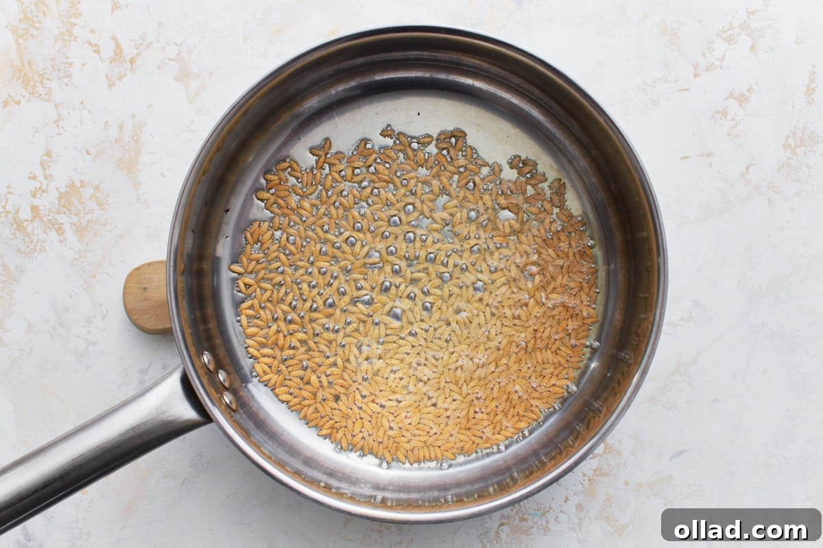 Flavorful Gluten-Free Rice Pilaf 6 Gluten-free orzo pasta being toasted in olive oil in a stainless steel pan until golden brown.