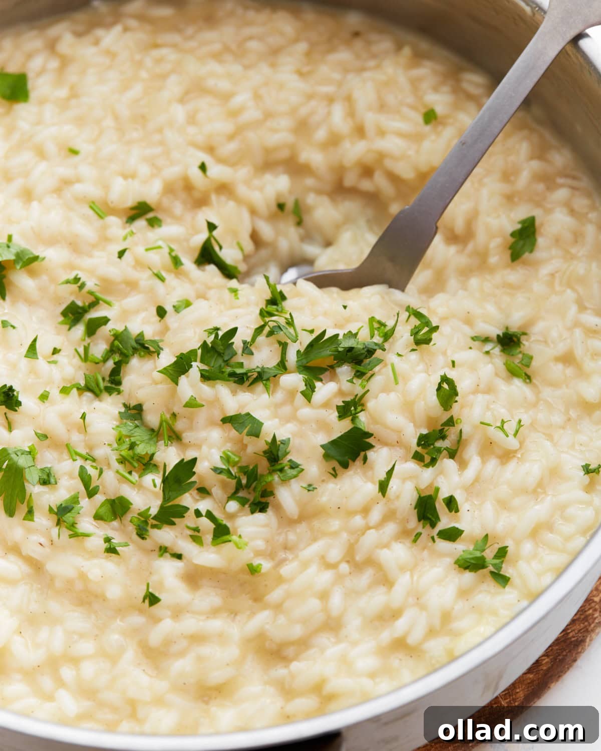 Creamy Gluten-Free Risotto 2 Creamy gluten-free risotto in a pan topped with chopped fresh parsley, with a serving spoon scooping from the center.