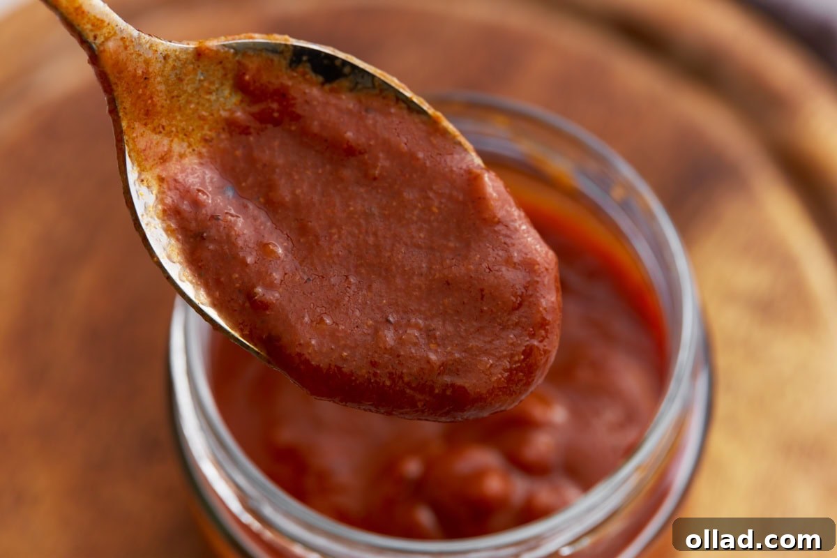 Close-up of a spoonful of thick, smooth enchilada sauce held over the jar.