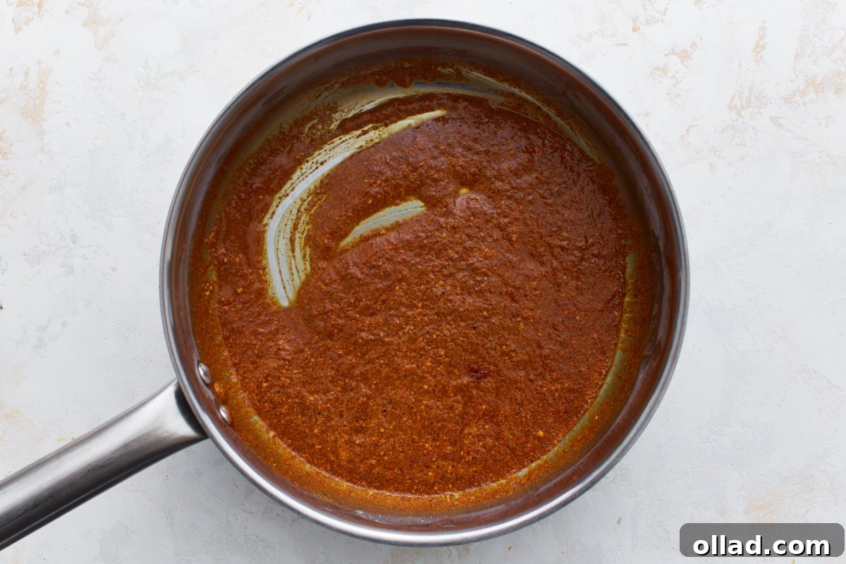 Spices blended into the roux in a saucepan, creating a thick, reddish-brown paste.