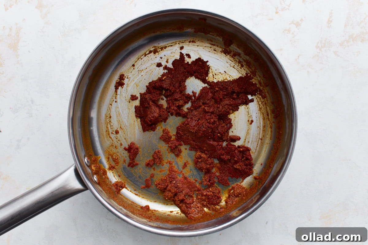 A saucepan with thick, deep red spiced tomato paste mixture before any liquid is added.