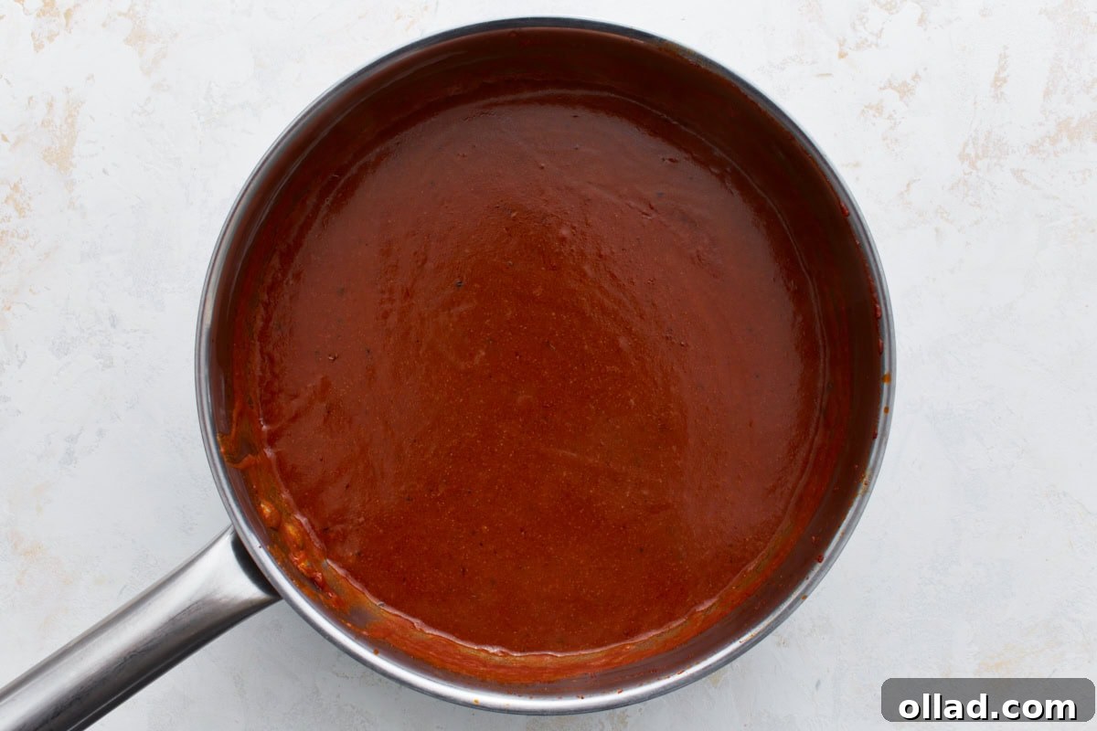 Enchilada sauce thickening in a saucepan, smooth and glossy with deep red color.