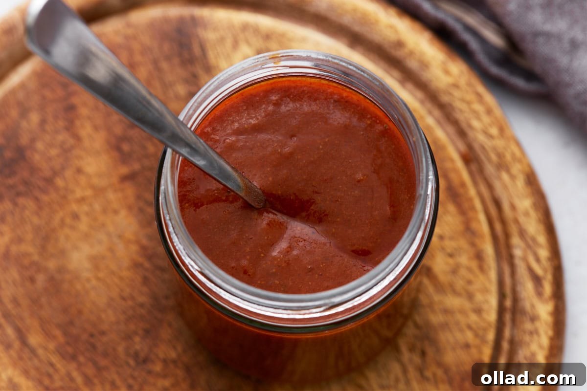 Top-down view of a jar filled with thick enchilada sauce, with a spoon dipped inside.