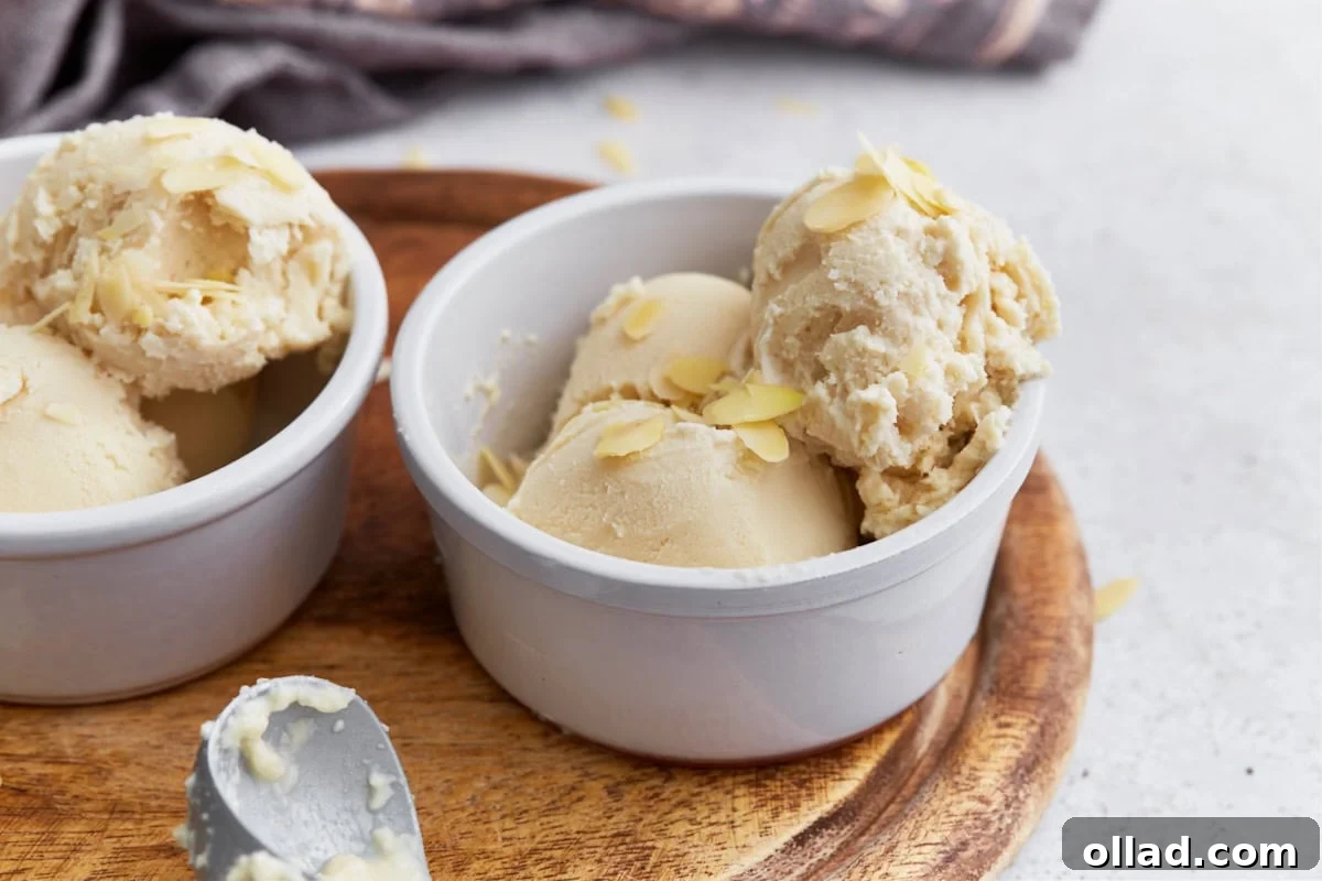 Side view of two bowls filled with almond milk ice cream, each topped with sliced almonds, presented on a rustic wood surface.