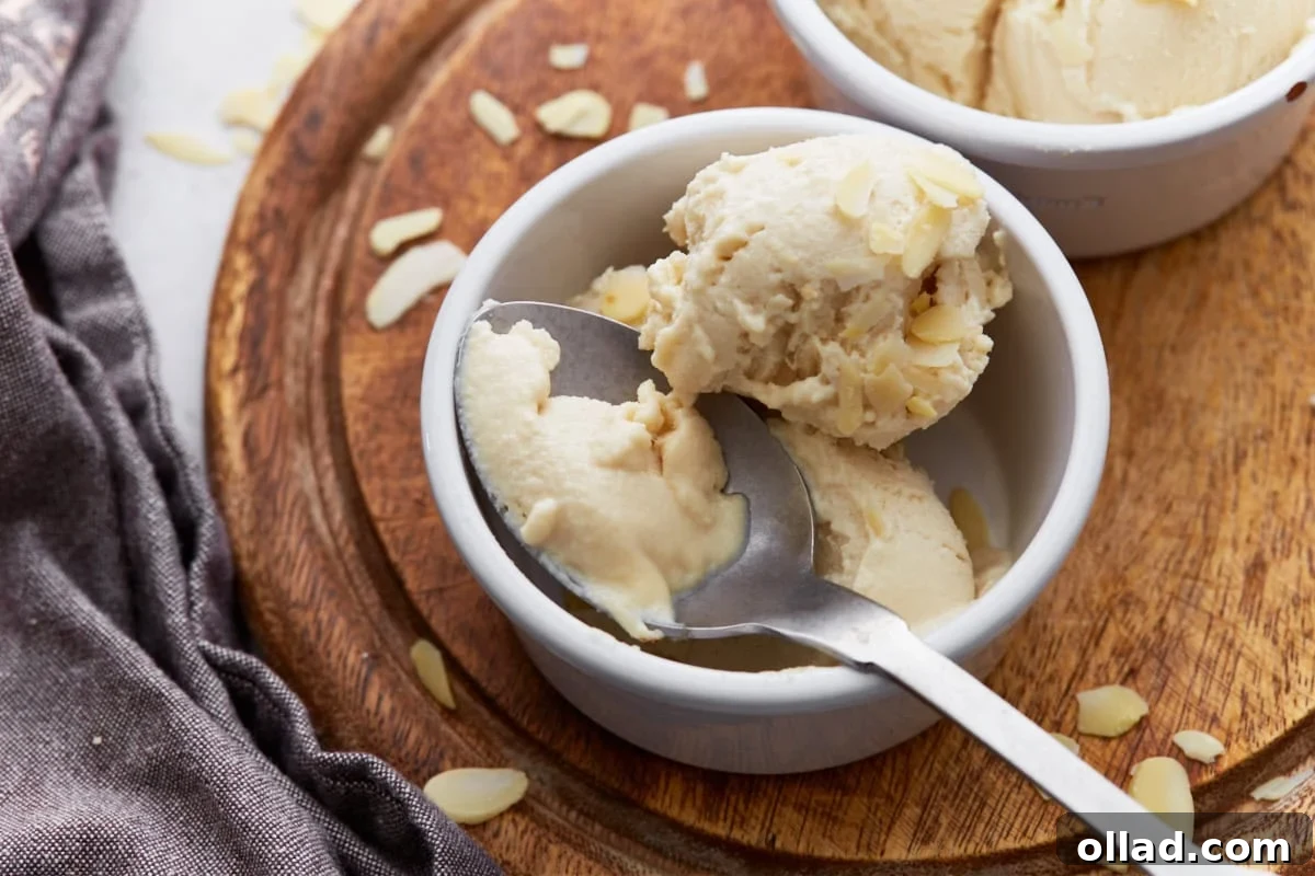 A spoonful of creamy almond milk ice cream being lifted from a ramekin, showcasing its smooth texture and topped with slivered almonds.