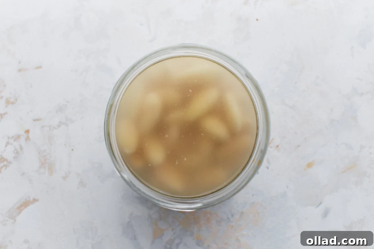 Top-down view of a glass jar filled with soaked blanched almonds in water, indicating the overnight soaking process.