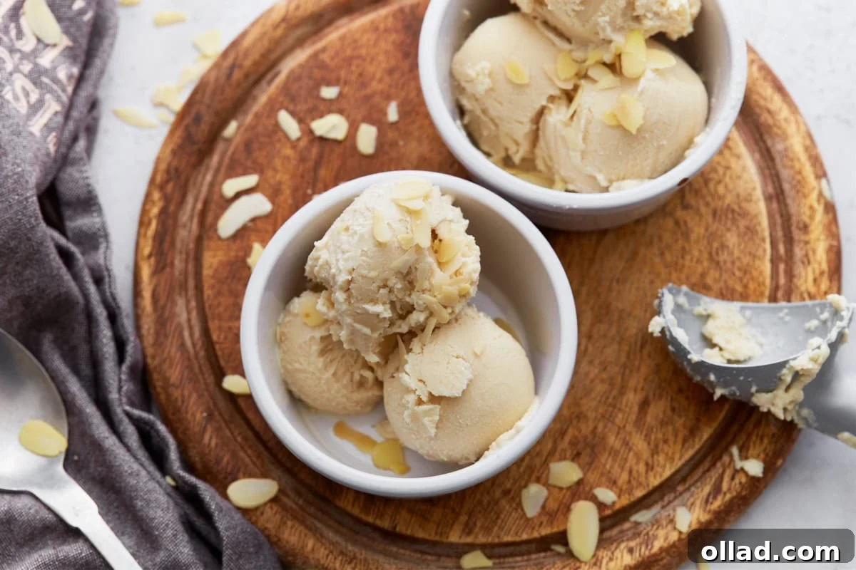 Two ramekins filled with scoops of almond milk ice cream on a wooden board, garnished with sliced almonds and a scoop resting on the side, ready to be served.
