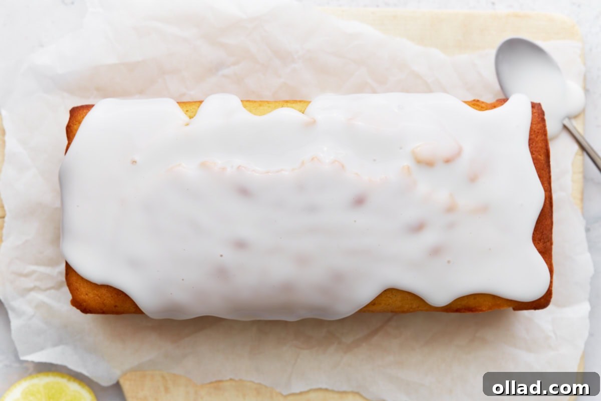 Gluten-Free Zesty Lemon Glaze Loaf 11 Iced lemon loaf on parchment paper with glaze spread evenly over the top.