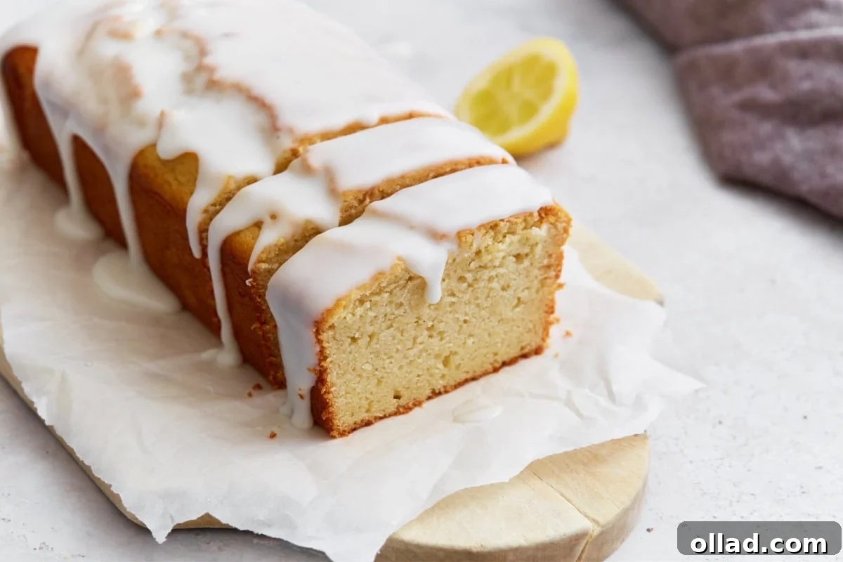 Gluten-Free Zesty Lemon Glaze Loaf 12 Sliced gluten-free iced lemon loaf on parchment paper, with a lemon half in the background and glaze dripping down the sides.