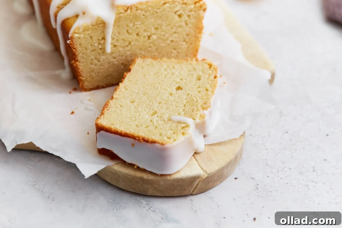 Gluten-Free Zesty Lemon Glaze Loaf 13 A single slice of gluten-free iced lemon loaf laid flat on parchment, showing the moist crumb and thick glaze along the edges.
