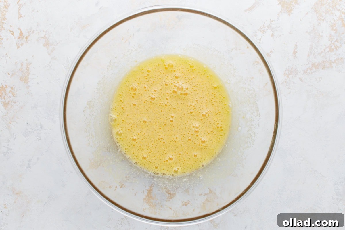 Gluten-Free Zesty Lemon Glaze Loaf 4 Whisked eggs and sugar in a clear glass bowl, lightly frothy and pale yellow.