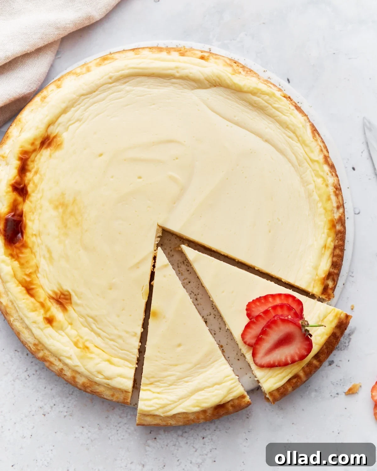 Whole baked keto cheesecake with one slice removed and garnished with fresh strawberry slices on a light background.