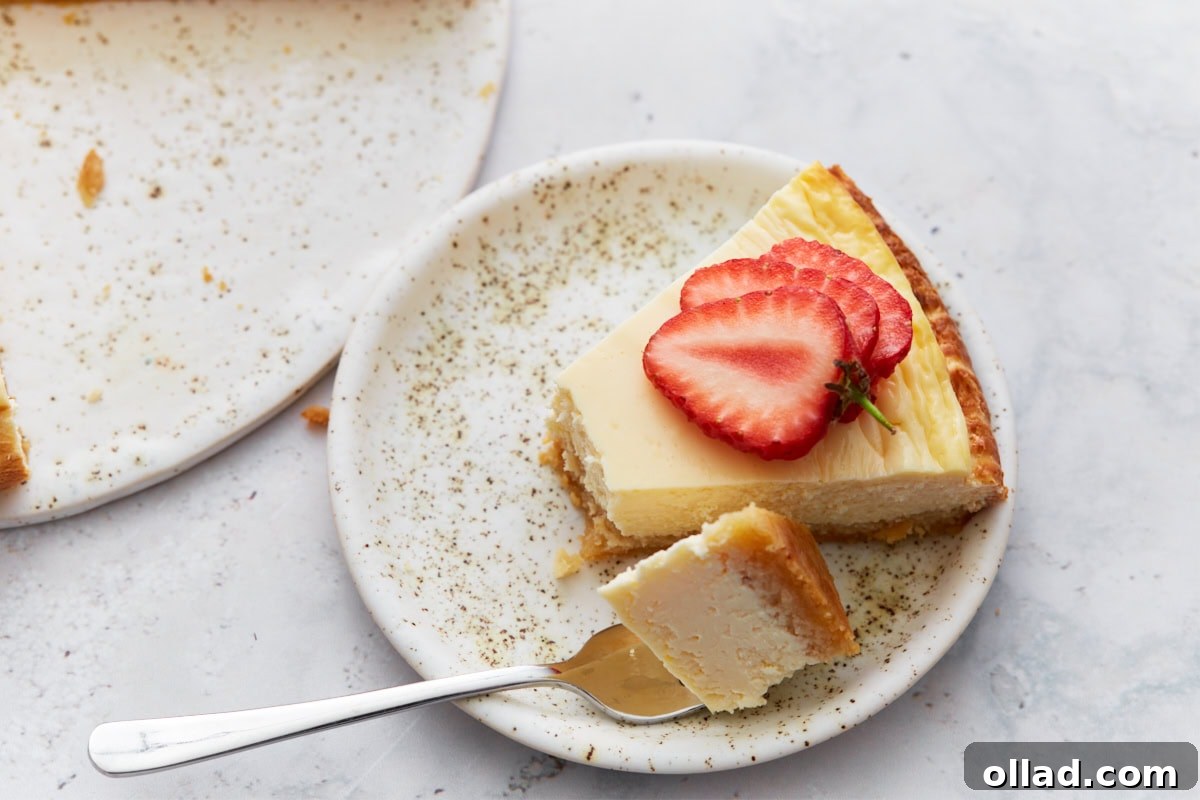 A single slice of keto cheesecake served on a speckled plate, topped with fresh strawberries and a bite taken with a fork.