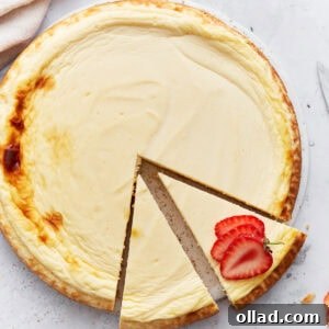 Whole baked keto cheesecake with one slice removed and garnished with fresh strawberry slices on a light background.