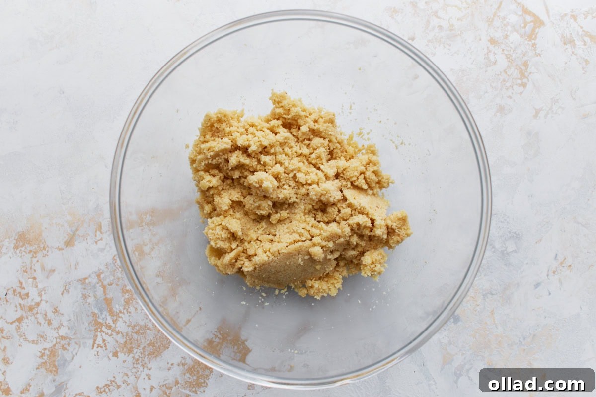 Crumbly almond flour crust dough mixture in a clear glass mixing bowl.