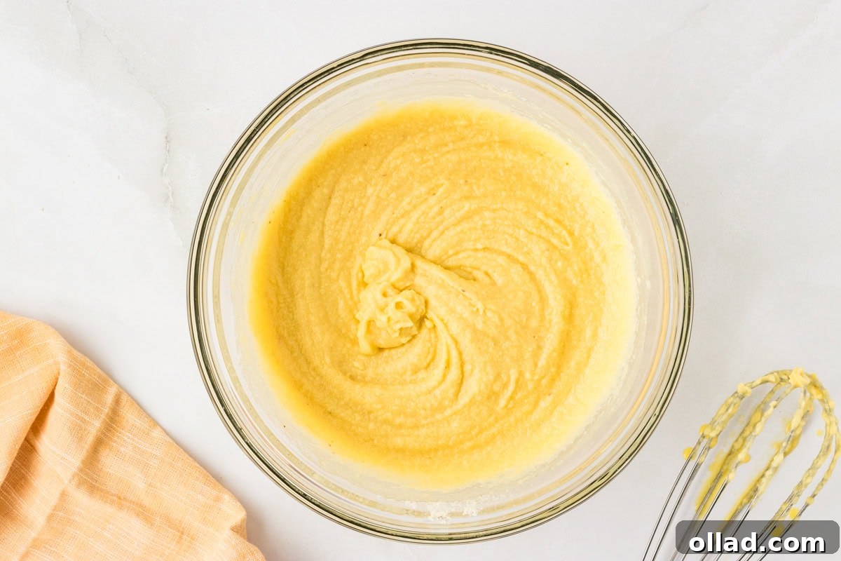 Ultimate Keto Cornbread 7 Smooth yellow cornbread batter in a glass bowl after mixing, with a whisk resting nearby.